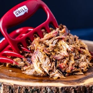 Meat shredder claws in shredded pulled pork on a wooden board.