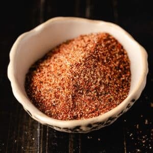 A white bowl filled with a brownish-red seasoning on a dark background.