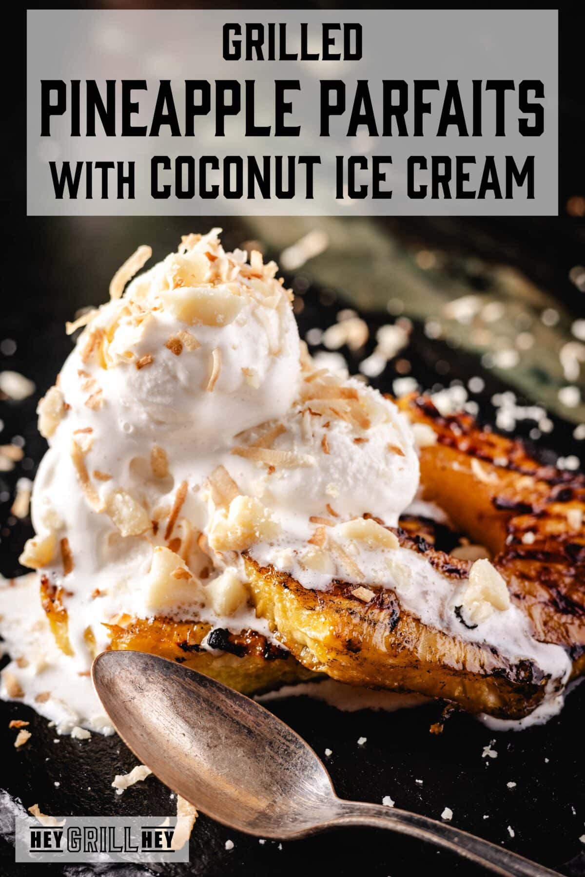 Grilled pineapple slices topped with ice cream and crumbled coconut on a black plate. The text overlay reads "Grilled Pineapple Parfaits with Coconut Ice Cream" at the top, and "Hey Grill Hey" at the bottom.